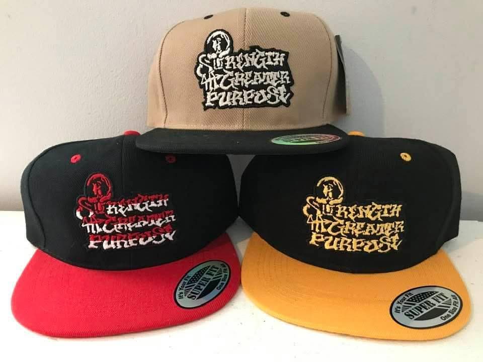 Three original H.E.R.O. embroidered snapbacks in tan and black, black and red, and black and gold